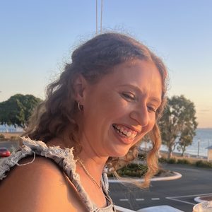Emma smiling on a balcony by the water at sunset.